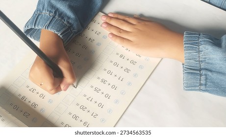 Close up student hands solves mathematics examples. The child holds the pencil in his hand. Notebook sheet with addition table examples. Kids education Concept.