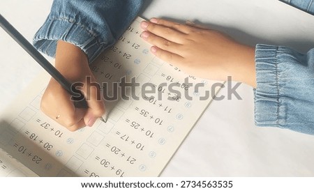 Close up student hands solves mathematics examples. The child holds the pencil in his hand. Notebook sheet with addition table examples. Kids education Concept.