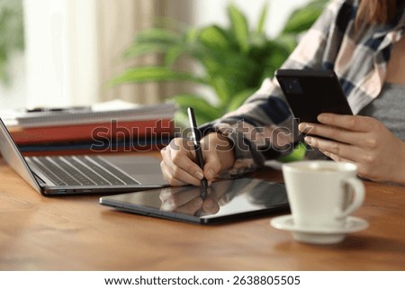 Close up of student hands using multiple devices taking notes on tablet at home