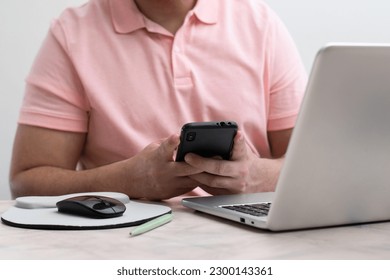 Close up of student using his cell phone front their laptop in white background