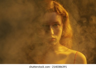Close up studio art portrait of beautiful redhead freckled woman posing in smoke, darkness and warm light