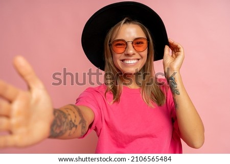 Close up studio photo of smiling young woman with tatoo on hands posing over pink background. 