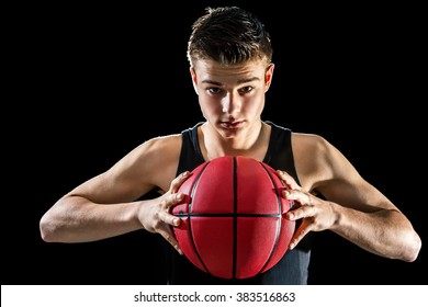 Close up studio portrait of handsome young basketball player holding inflated orange ball.Isolated against black background.