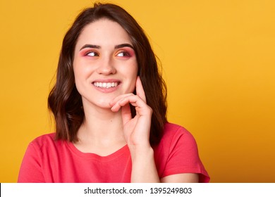 Close up studio portrait of pretty lovely charming lady looking away, keeps hand under chin, trying to understand or remember something, has bright make up, posing isolated over yellow background. - Shutterstock ID 1395249803