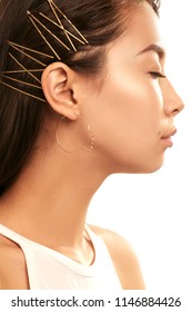 Close up studio portrait of a young Asian lady wearing abstract face-shaped hoop earrings. The side view of the brunette girl with slicked back hair with bobby pins, posing with her eyes closed.