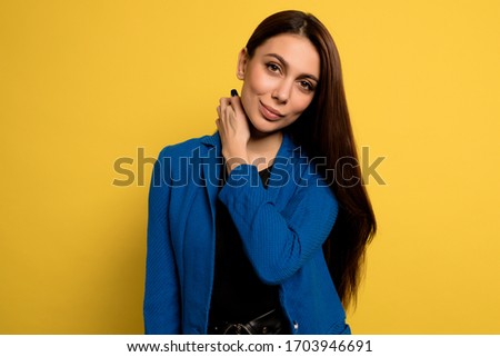 Close up studio shot adorable lovely woman in blue jacket posing with smile over yellow background. European female model posing for studio portrait