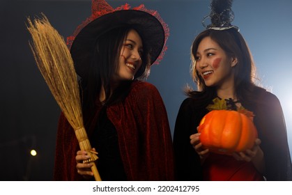 Close Up Studio Shot Of Asian Young Happy Beautiful Teenager Girl Wearing Halloween Costume With Tall Witch Hat And Woman Friend Standing Smiling Dancing In Traditional Trick And Treat Party At Night.