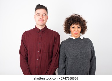 Close Up Studio Shot Of Beautiful Young Mixed Race Couple Model With Curly Dark Hair Looking At Camera With Charming Cute Smile While Posing Against White Blank Copy Space Wall For Your Content