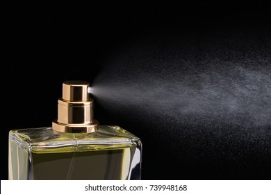 Close Up Studio Shot Of Cosmetic Perfume In Glass With The Nozzle Spraying And Splashing On Black Background