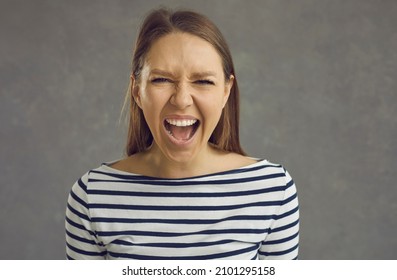 Close up studio shot of a crazy stressed beautiful young woman with an angry displeased face expression screaming loudly at the camera. Portrait of a mad girlfriend or enraged school teacher - Shutterstock ID 2101295158