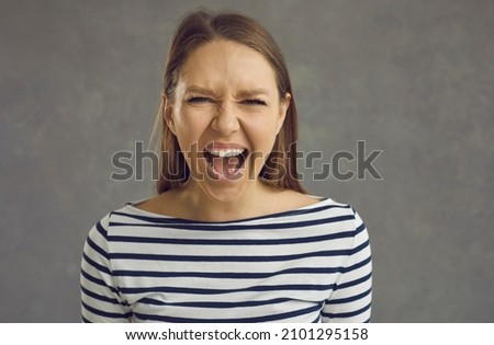 Close up studio shot of a crazy stressed beautiful young woman with an angry displeased face expression screaming loudly at the camera. Portrait of a mad girlfriend or enraged school teacher