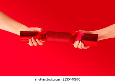 Close Up Studio Shot Of Female Hands Pulling Christmas Cracker Against Red Background