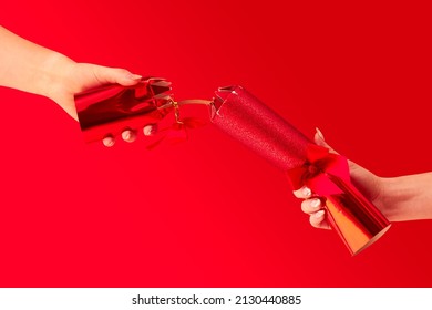 Close Up Studio Shot Of Female Hands Pulling Christmas Cracker Against Red Background