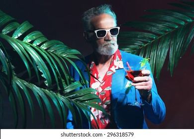 Close Up Stylish Middle Aged Businessman With Sunglasses Holding A Cocktail Drink Between Indoor Palm Trees During A Tropical Party At Night