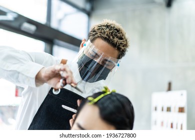 Close Up Of Stylist Asian Male Hairdresser Wearing A Face Shield And Mask For Protection And Practicing Social Distance During Covid 19 Pandemic Giving Haircut Service To Male Customer In Modern Salon