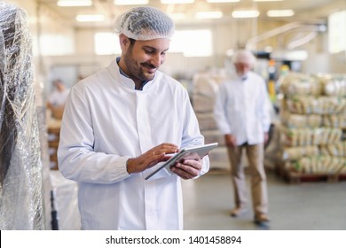 Close Up Of Supervisor In Uniform Using Tablet For Checking Data While Standing In Food Factory.