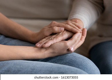 Close up of supportive grownup female hold senior mother hands showing lover and care, adult daughter comfort caress middle-aged mum talking sharing secrets, having close intimate moment at home