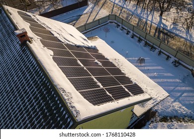 Close Up Surface Of A House Roof Covered With Solar Panels In Winter With Snow On Top. Energy Efficiency And Maintenance Concept.