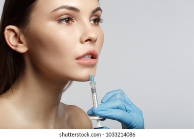 Close up of surgeon hand in glove injecting female lips by silicon liquid. Calm woman is looking forward with serenity. Isolated and copy space