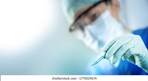 close up of the surgeon's hand holding a scalpel and blurred female doctor's face in the background with copy space, concept of surgical operations, hospitals and clinic staff - Shutterstock ID 1775019674