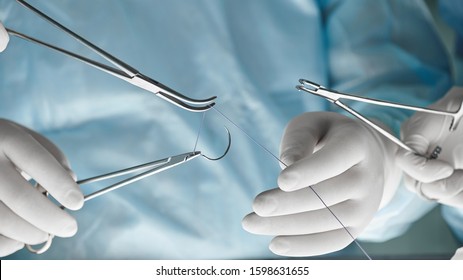 Close Up Of Surgical Team Hands, Surgeon Holding Needle Holder And Suture Material. Suture Thread. Nylon Surgical Thread. Needle Holer And Suture Material In Operating Room,medical Concept.