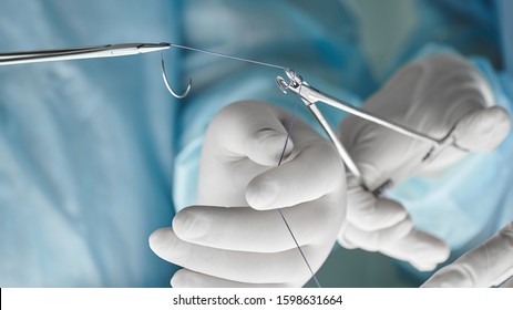 Close up of surgical team hands, surgeon holding needle holder and suture material. Suture thread. Nylon surgical thread. Needle holer and suture material in operating room,medical concept.