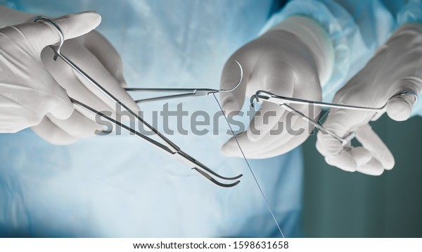 Close\
up of surgical team hands, surgeon holding needle holder and suture\
material. Suture thread. Nylon surgical thread. Needle holer and\
suture material in operating room,medical\
concept.