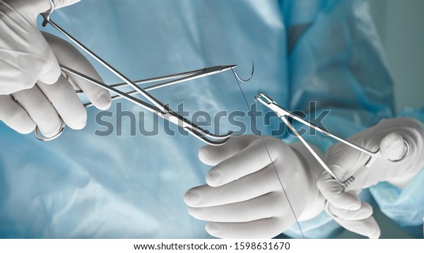Close\
up of surgical team hands, surgeon holding needle holder and suture\
material. Suture thread. Nylon surgical thread. Needle holer and\
suture material in operating room,medical\
concept.