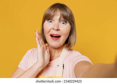 Close Up Surprised Elderly Housekeeper Housewife Woman 50s In Orange Apron Doing Selfie Shot Pov On Mobile Phone Hold Face Isolated Plain On Yellow Background Studio People Household Lifestyle Concept