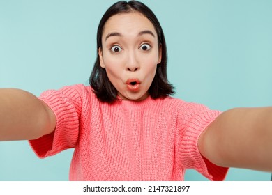 Close Up Surprised Young Amazed Woman Of Asian Ethnicity 20s In Pink Sweater Doing Selfie Shot Pov On Mobile Phone Isolated On Pastel Plain Light Blue Color Background Studio. People Lifestyle Concept