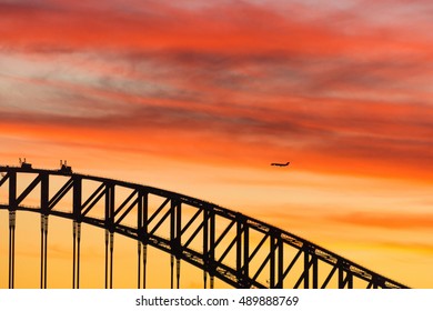 Close Up Of Sydney Harbour Bridge Structure Against Dramatic Sunset Sky On The Background. Black Silhouette Of Plane And Urban Architecture