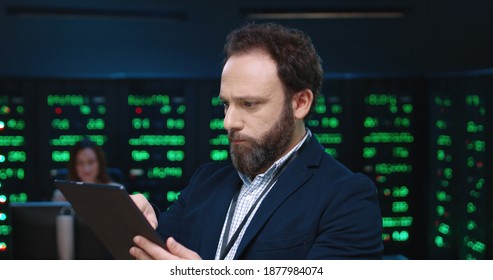 Close up of system administrator programmer in jacket working on tablet standing in office on background of working servers.