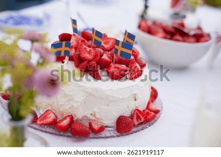 A close up of a table set with a cake of strawberries and whipped cream and a bowl of straberries in the background