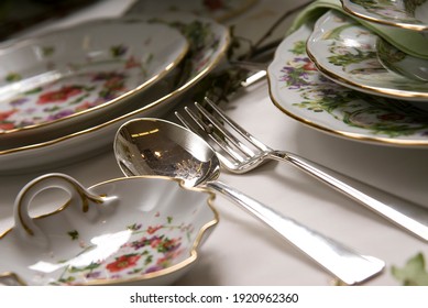 Close up of a table set up with colorful porcelain dining set and silverware for a special occasion meal.  Gold painting on the edges.