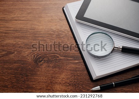 Close up Tablet Gadget and Magnifying Glass on Top of Open Notes, Resting on Wooden Table at the Right Edge, with Copy Space on Left Side for Texts.