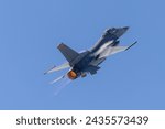 Close tail view of a F-16 Fighting Falcon in a high G maneuver, with condensation streaks at the wing roots and afterburner on 