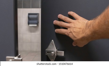 Close Up Of Tan Hairy Man Hand Pushing Open A Grey Blue Bathroom Stall Door From Inside Under A Warm Light Front Point Of View Perspective Angle.