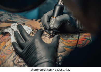 Закройте тату-машинку. Татуаж. Человек создает рисунок на спине профессиональным татуировщиком.