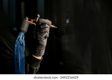 Close up tattoo master hand in black gloves holding a tattoo machine on black background. Copy space for your text