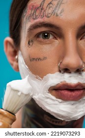 Close Up Of Tattooed Young Man With Shaving Foam On Face Holding Vintage Brush Isolated On Blue 