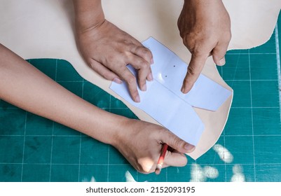 Close up teacher hand is teaching a leather sewing making student how to do vest drafting pattern template on leather at   crafting class, young new start up learning to start leather making business