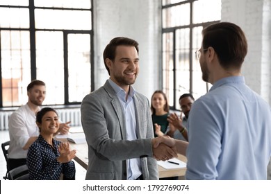 Close up team leader thanking successful employee for good work at meeting, diverse colleagues applauding, cheering, executive shaking smiling businessman hand, congratulating with promotion - Powered by Shutterstock