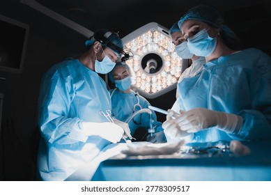 Close teamwork of surgeons performing operation in operating theater, medical staff in sterile uniforms, advanced surgery and healthcare concept