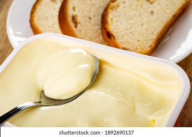 Close Up Of Teaspoon In Plastic Box With Creamy Cheese, Slices Of Bread With Raisin In Plate On Wooden Table