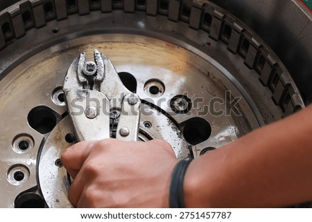 Close up of a technician hand using locking pliers to grip a metal bolt on a heavy machinery industrial component during repair or maintenance work.