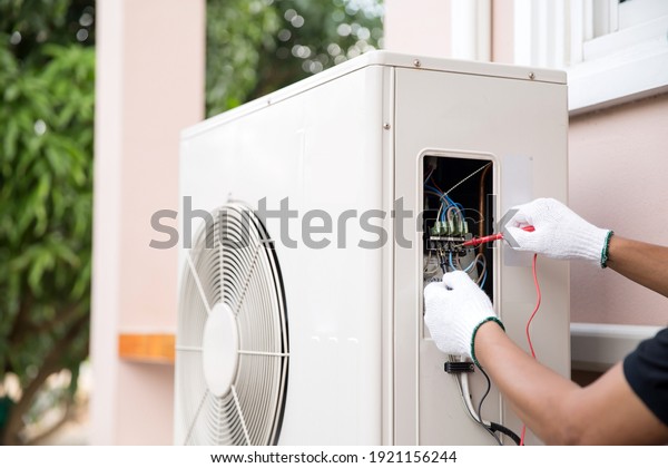 Close up technician hand using measuring
equipment checking electric current voltage at circuit breaker on
outdoor air compressor unit after installation and air conditioner
services maintenance