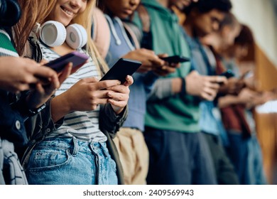 Close up of teenage girl and her friends using mobile phones at high school hallway. - Powered by Shutterstock