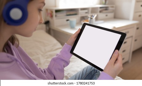 Close up teenage girl wearing headphones looking at white empty mockup tablet screen, watching video or webinar, playing mobile device game, chatting in social network online, making video call - Powered by Shutterstock