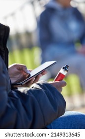 Close Up Of Teenagers With Mobile Phone Vaping  In Park