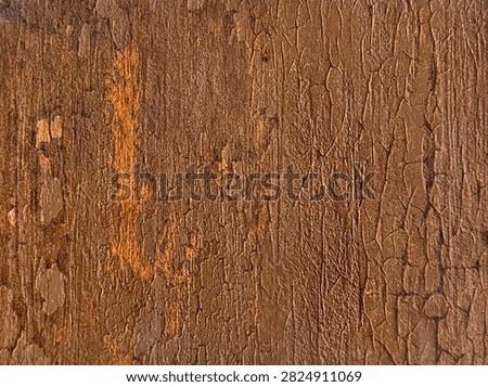 Close up texture of corroded rustic metal featuring heavily cracked brown paint, fine fissures, and bright orange rust patches.